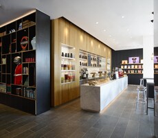 Ein modernes Café mit einer Holztresen, Regalen mit Kaffeemaschinen und einer Auswahl an Gebäck.