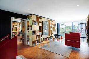 Una biblioteca moderna con estanterías, un sillón rojo y una partición de vidrio.