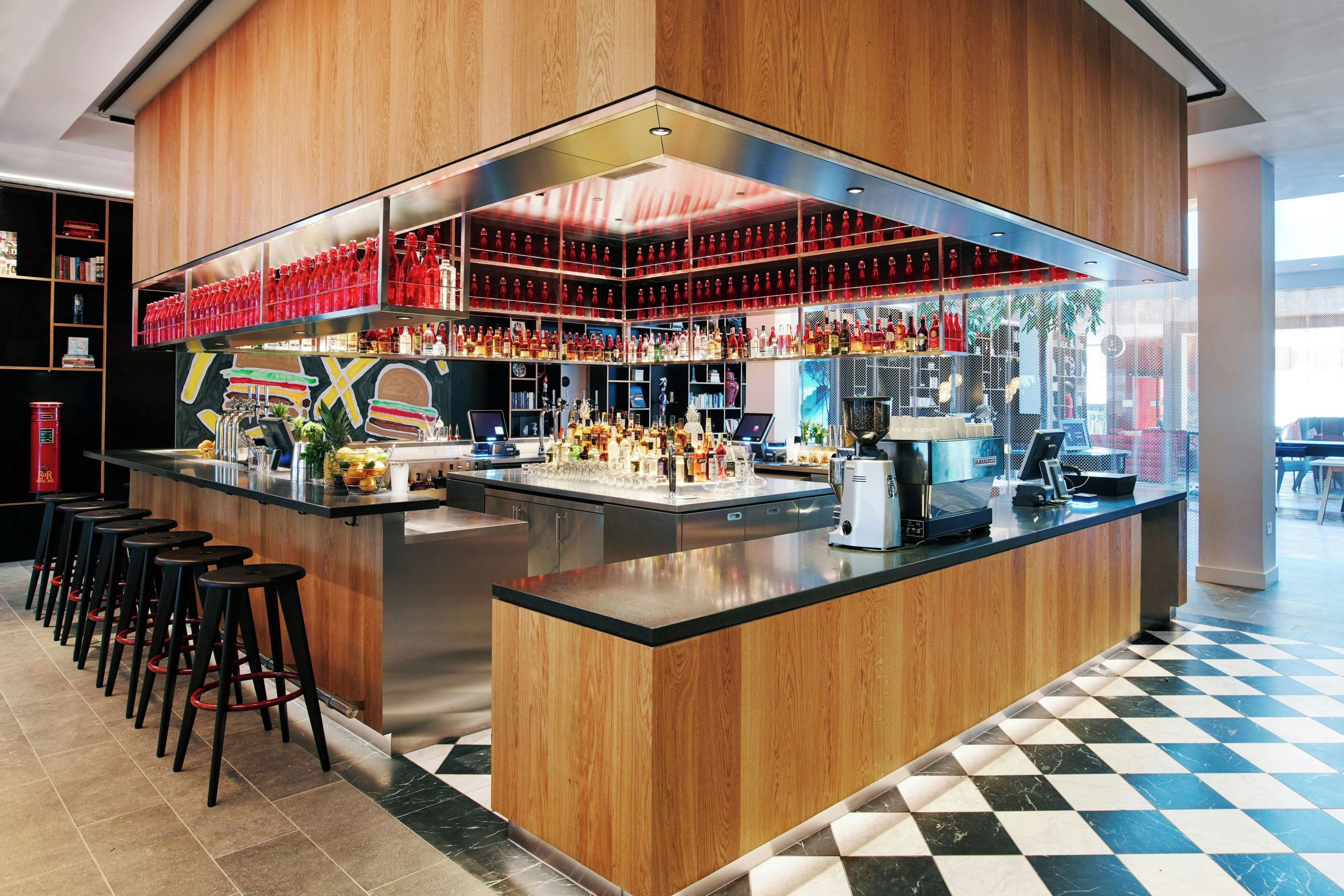 Uma área de bar com chão xadrez, balcão central e banquetas.