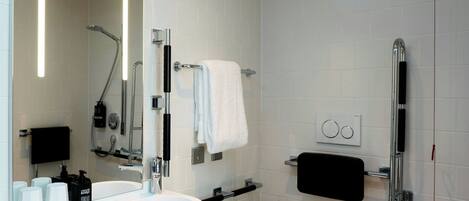 Et moderne badeværelse med vask, toilet, bruser og stort spejl.