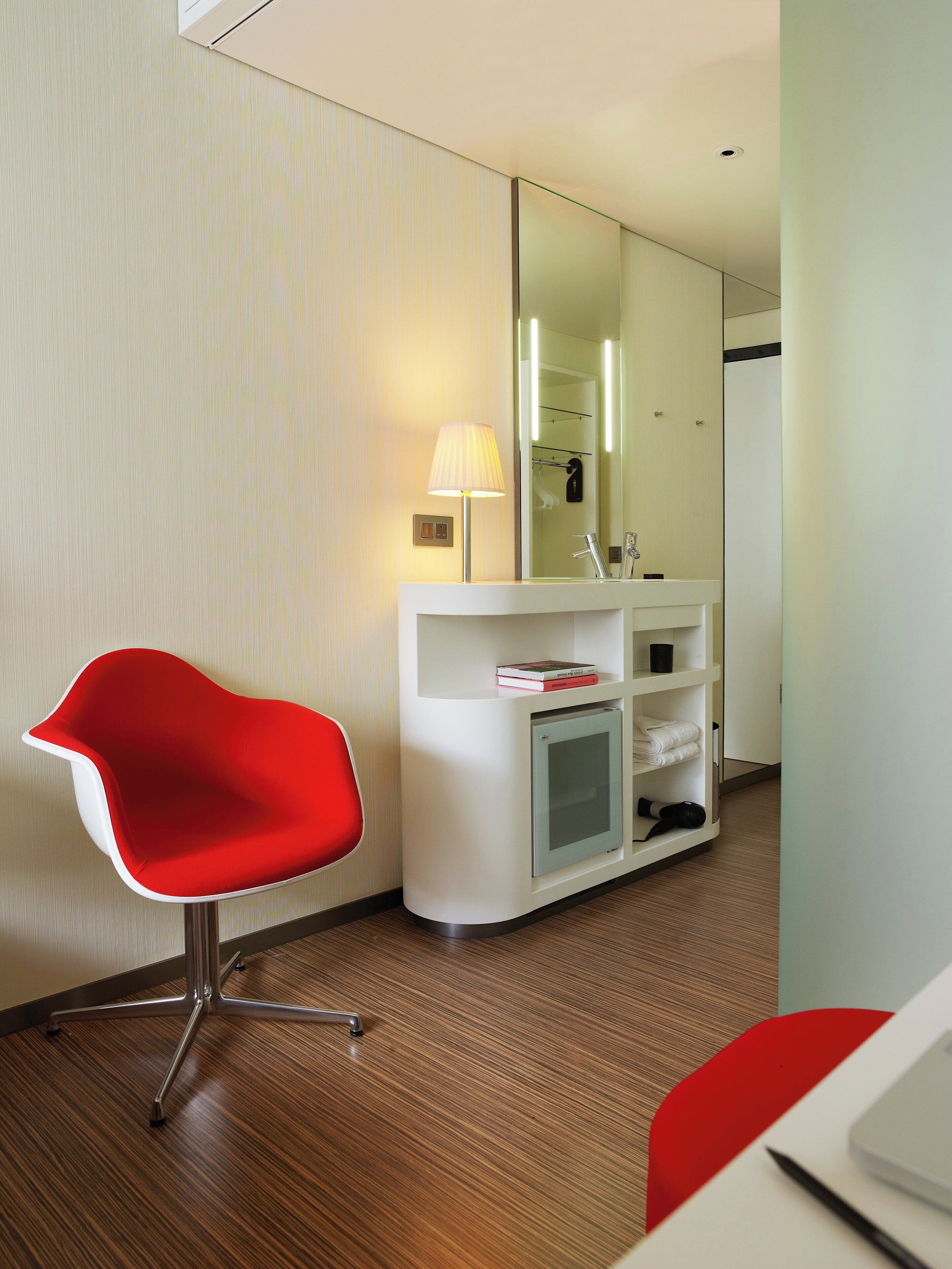A modern bathroom with a white vanity, a red chair, and a mirror.