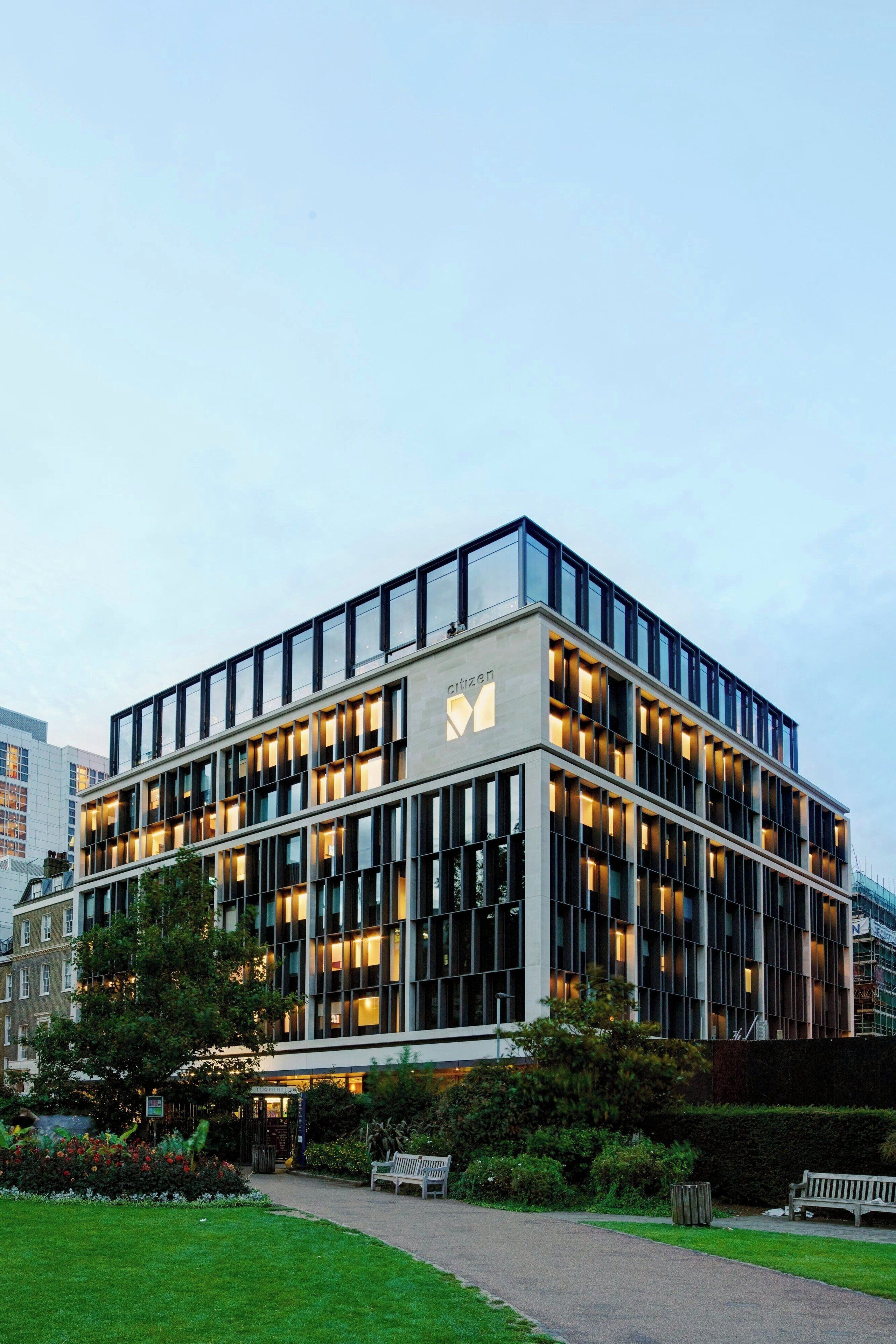 A modern building with a glass facade, multiple floors, and a well-maintained garden area with benches.