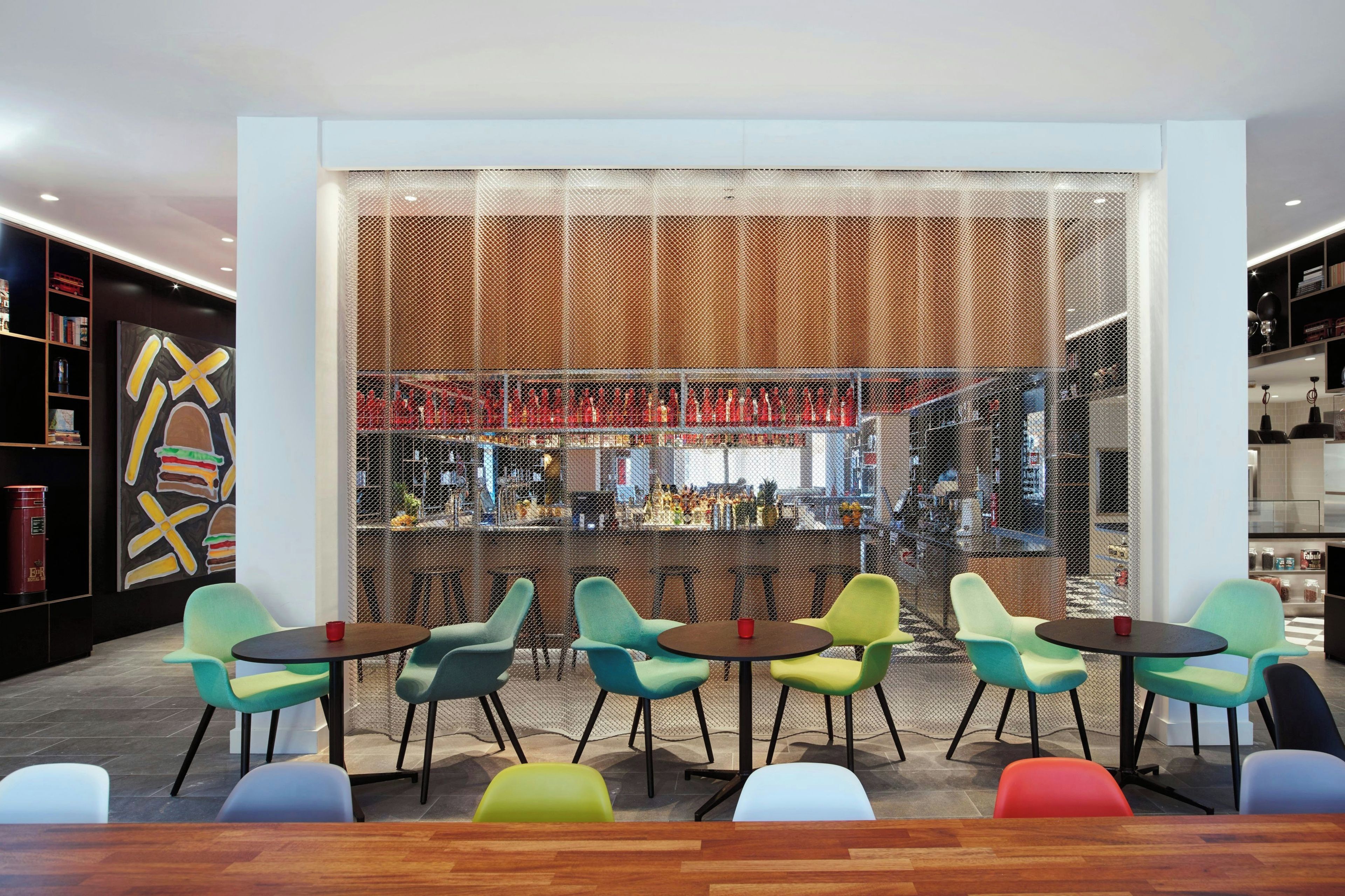 A modern bar area with colorful chairs, a bar counter, and a decorative wall with a geometric pattern.
