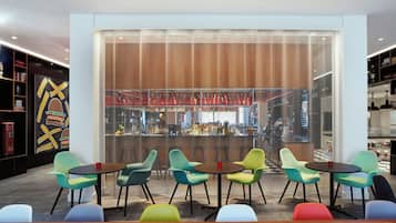 A modern bar area with colorful chairs, a bar counter, and a decorative wall with a geometric pattern.