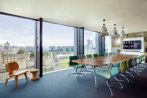 A conference room with a large table, multiple chairs, and a view of a cityscape through large windows.