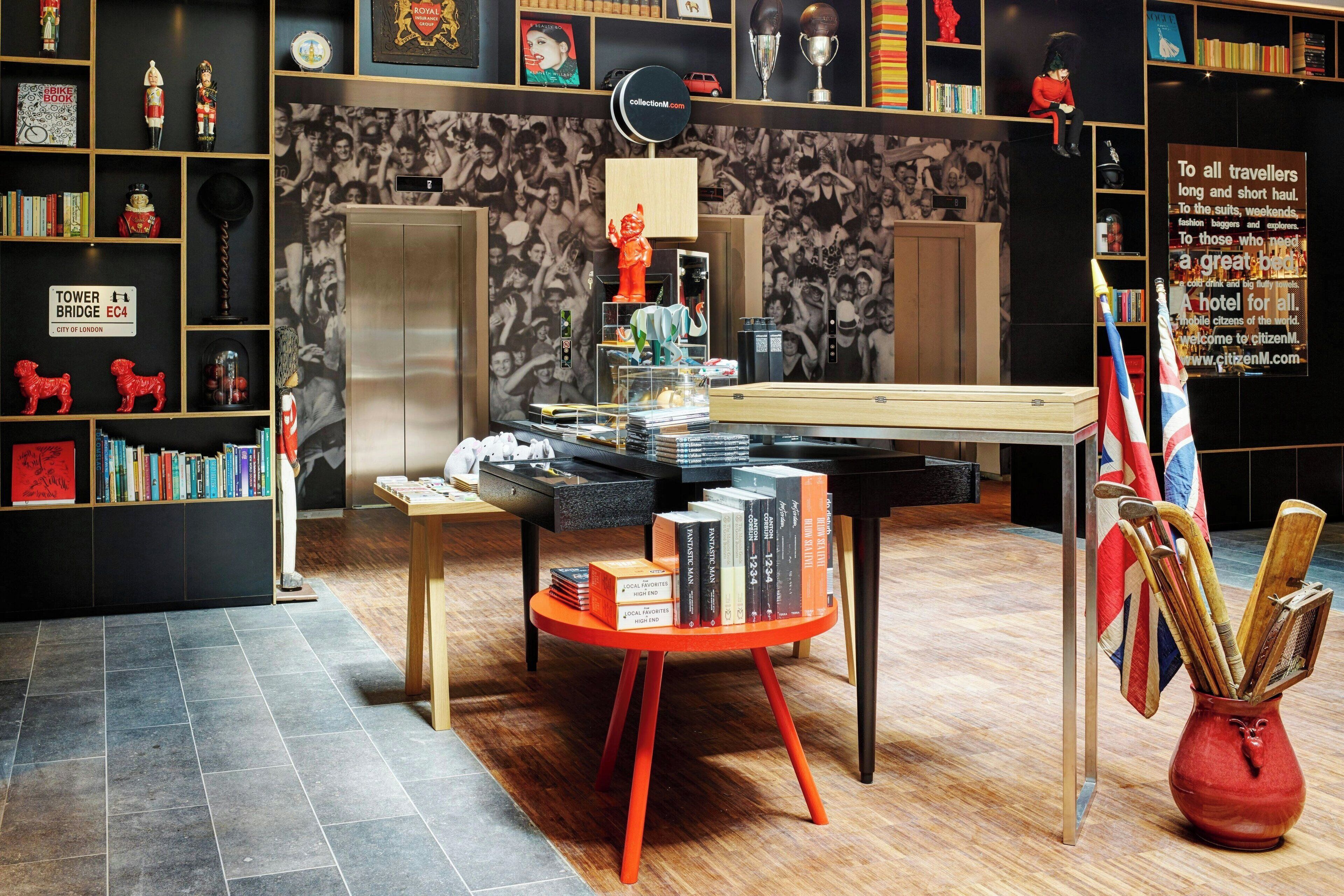 A hotel lobby with a central table displaying books, a red vase with walking sticks, and a backdrop of black and white photographs.