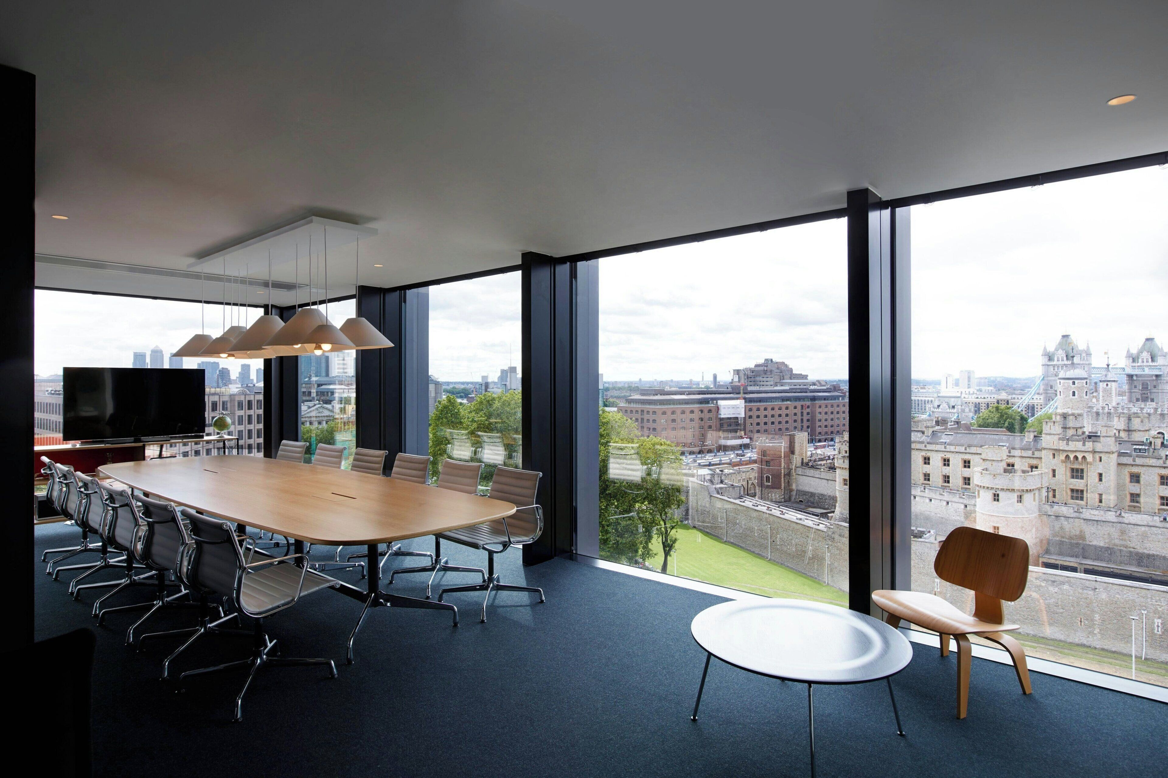 A modern conference room with a large table, chairs, and a television. It features large windows with a city view.