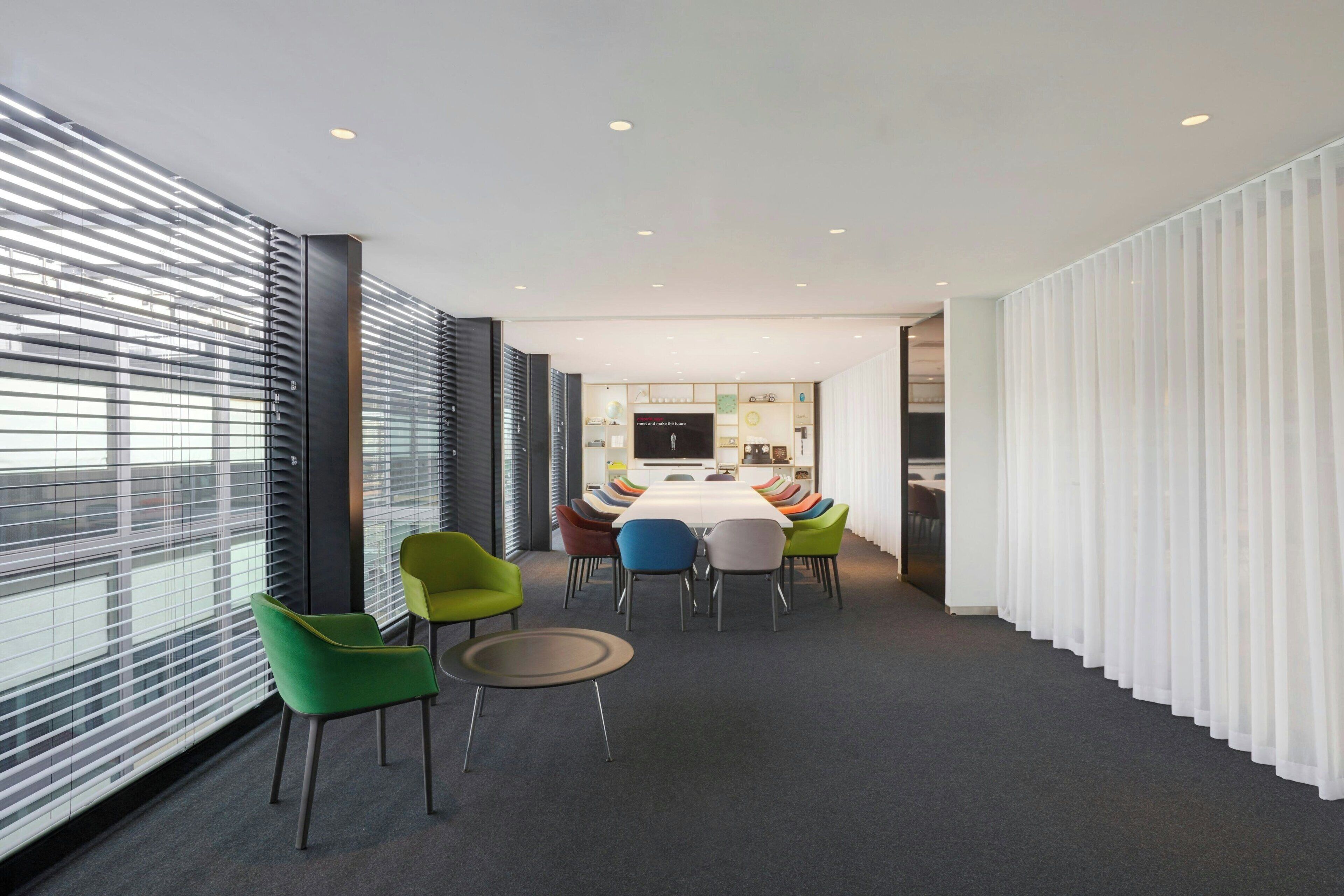 Une salle de réunion moderne, dotée d’une longue table, de chaises colorées et d’un grand écran.
