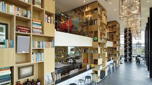 A modern library with bookshelves, a bar area, and a view of the city. - citizenM Tower of London (London)