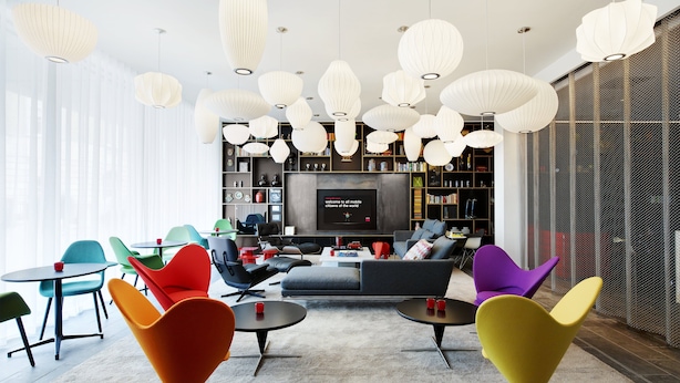 A modern living room with a large TV, colorful chairs, and a bookshelf. - citizenM Tower of London (London)
