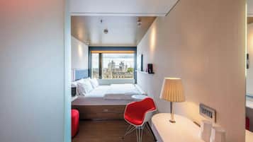 Una habitación de hotel moderna con una cama, una silla roja, un escritorio y una lámpara.
