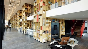 A modern library with high ceilings, wooden bookshelves, and a cozy seating area with leather chairs and a cowhide rug. - citizenM Tower of London (London)
