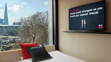 Une chambre d’hôtel avec une grande fenêtre, un lit avec une literie blanche, deux oreillers et un téléviseur affichant un message.