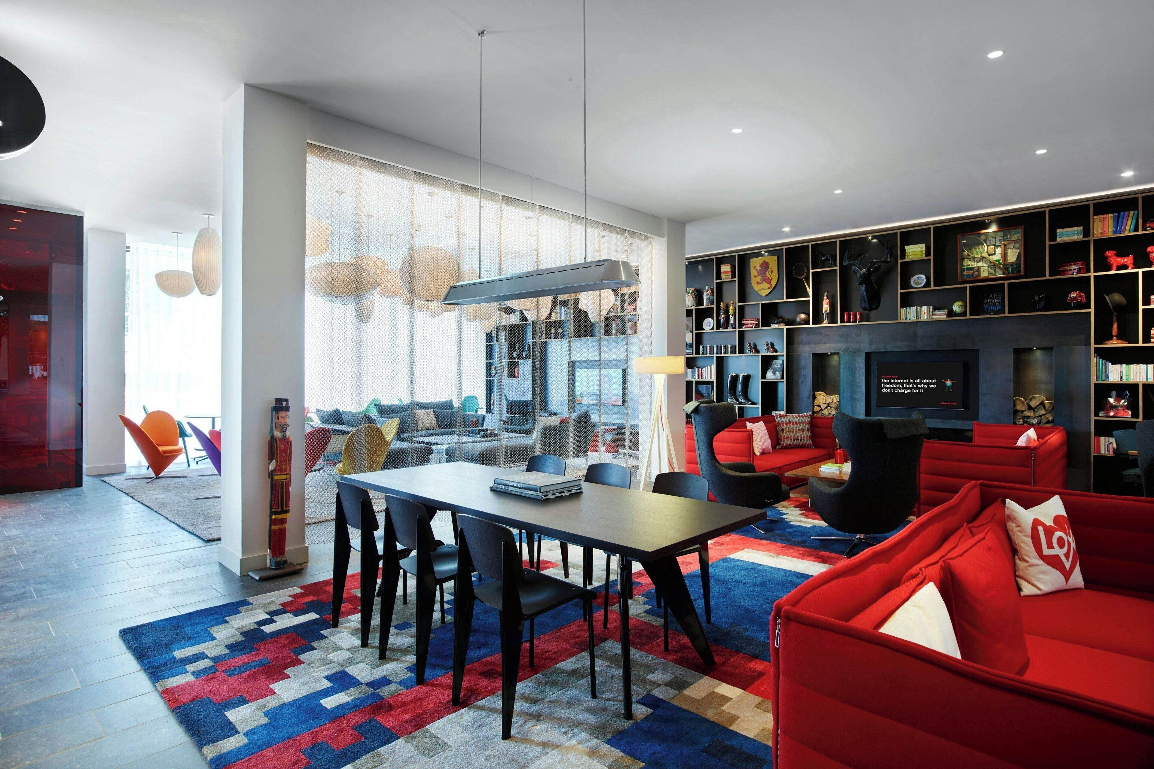 A modern living room with a dining area, red sofas, and a bookshelf filled with books and decorative items.