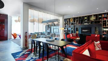 A modern living room with a dining area, red sofas, and a bookshelf filled with books and decorative items.