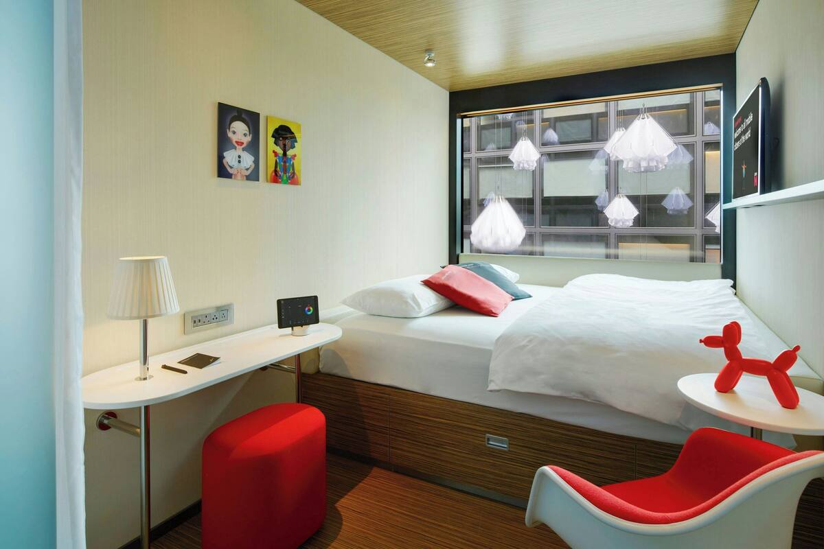 A modern hotel room with a bed, a desk, a chair, and a window with curtains.