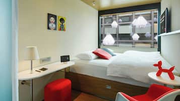 Una camera d'albergo moderna con un letto, una scrivania, una sedia e una finestra con tende.