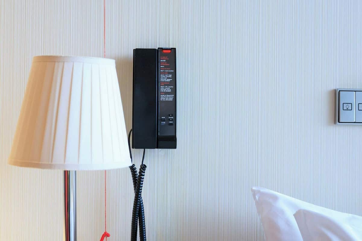 A hotel room with a round table, a lamp, a telephone, and a bed.