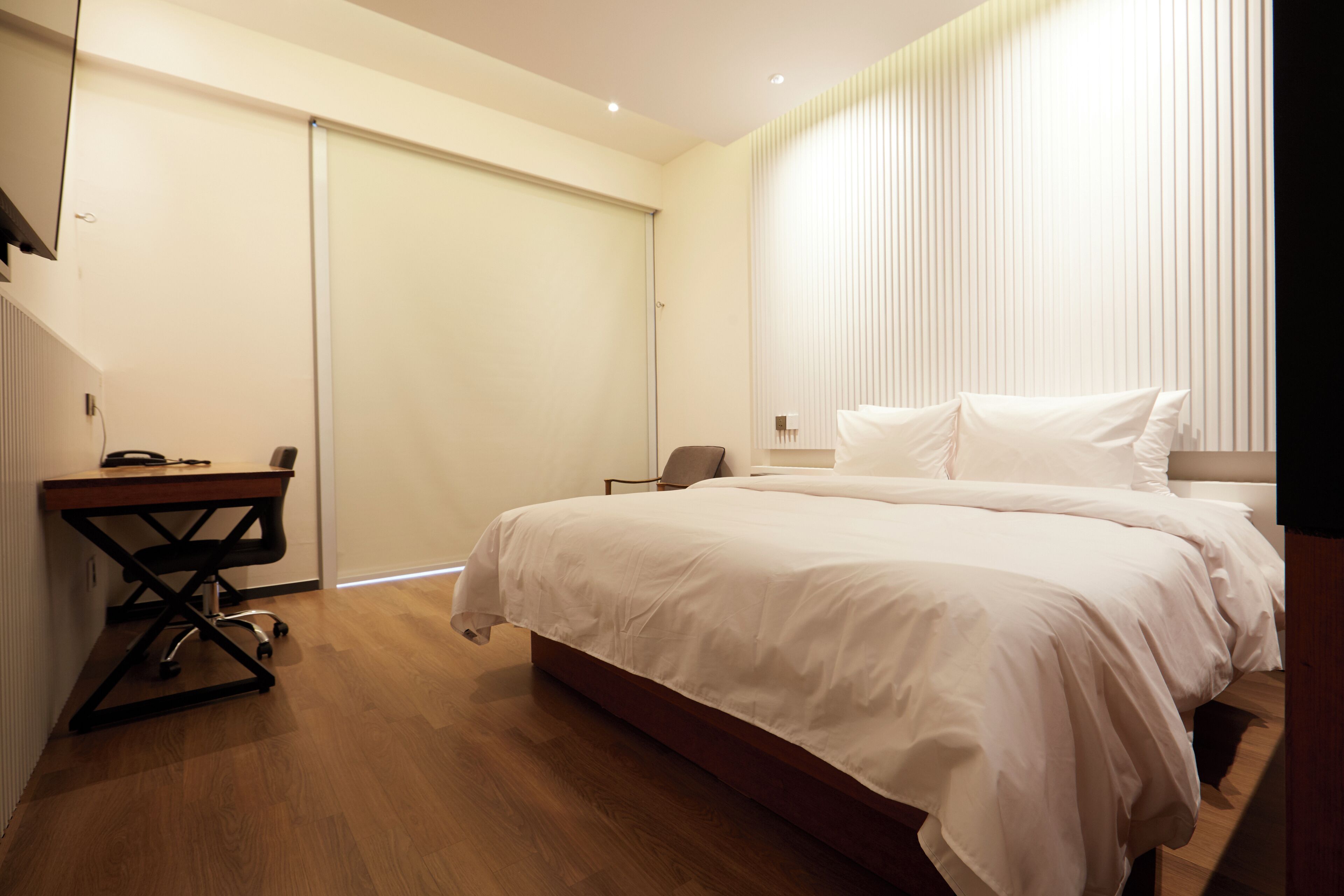 A modern bedroom with a large bed, a desk, and a chair.