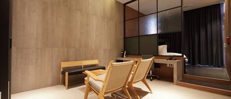 A modern hotel room with a large mirror, a wooden desk, two chairs, and a bench.