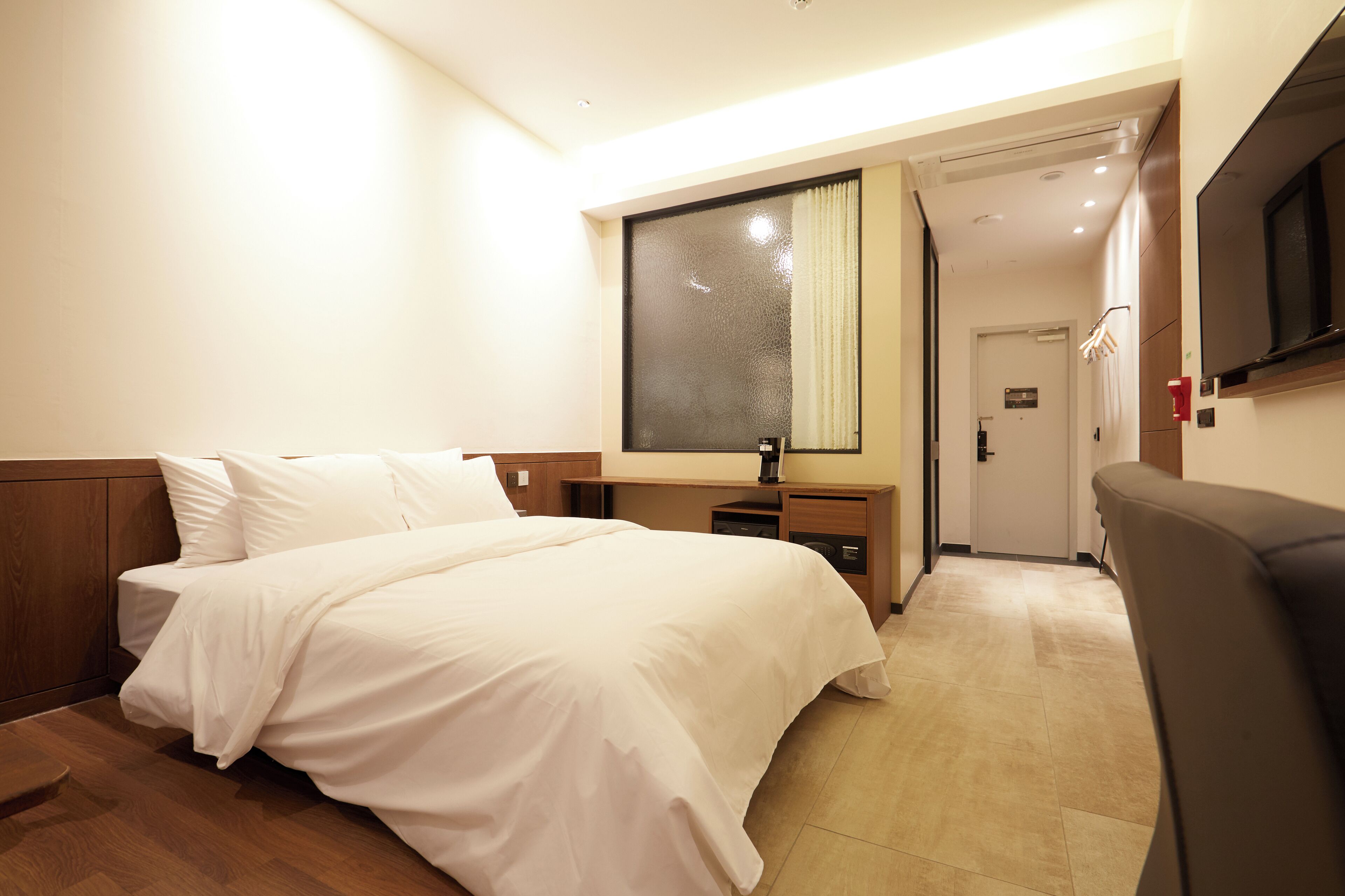 A hotel room with a large bed, a desk, a chair, a TV, and a window with curtains.