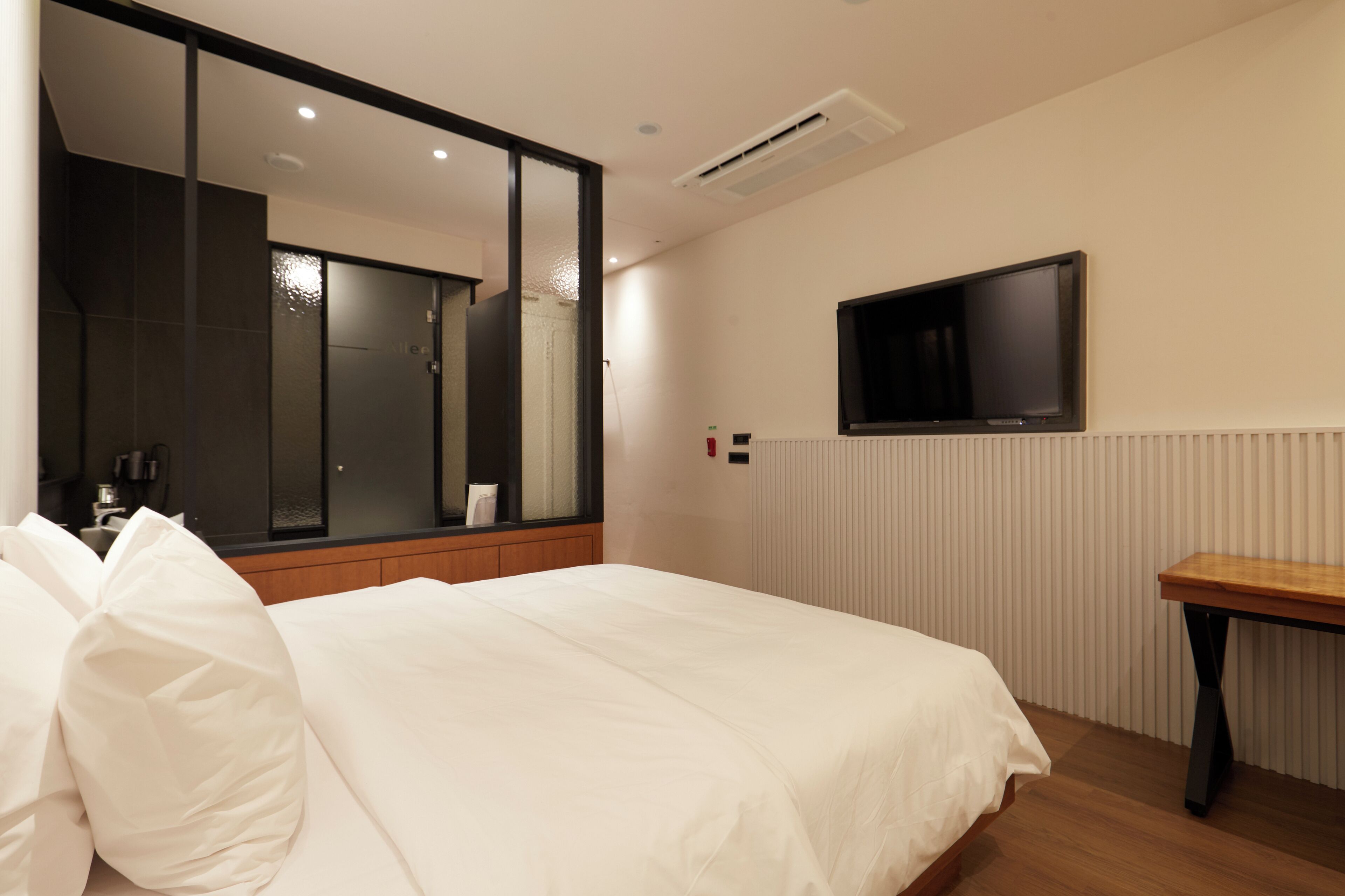 A hotel room with a large bed, a bedside table, a TV mounted on the wall, and a mirror.