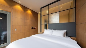 Ein modernes Hotelzimmer mit einem großen Bett, Wandverkleidung aus Holz, einer Glasabtrennung und Blick auf die Stadt.