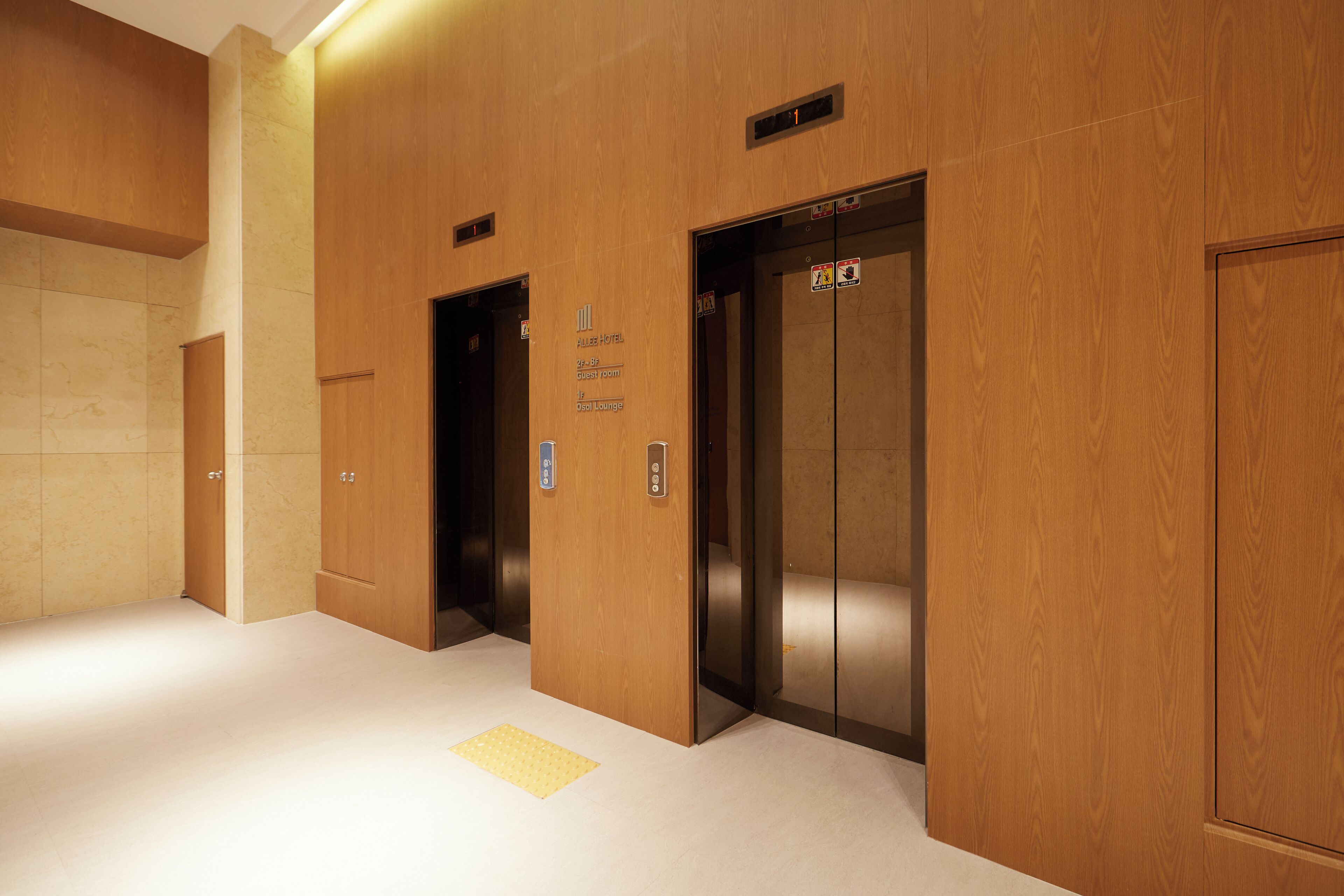 An elevator area with wooden paneling, a sign for the Plaza Hotel, and a yellow tactile paving.
