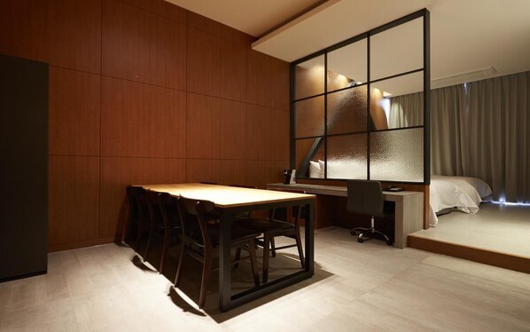 Une chambre d’hôtel moderne avec un mur en bois, un bureau avec des chaises, un lit et une grande fenêtre dotée de panneaux en verre dépoli.