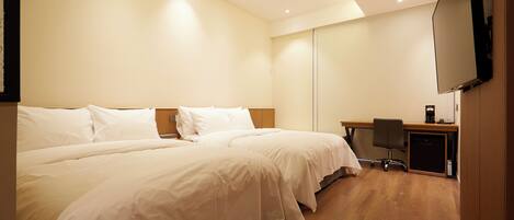 A hotel room with two beds, a desk, a chair, and a TV mounted on the wall.
