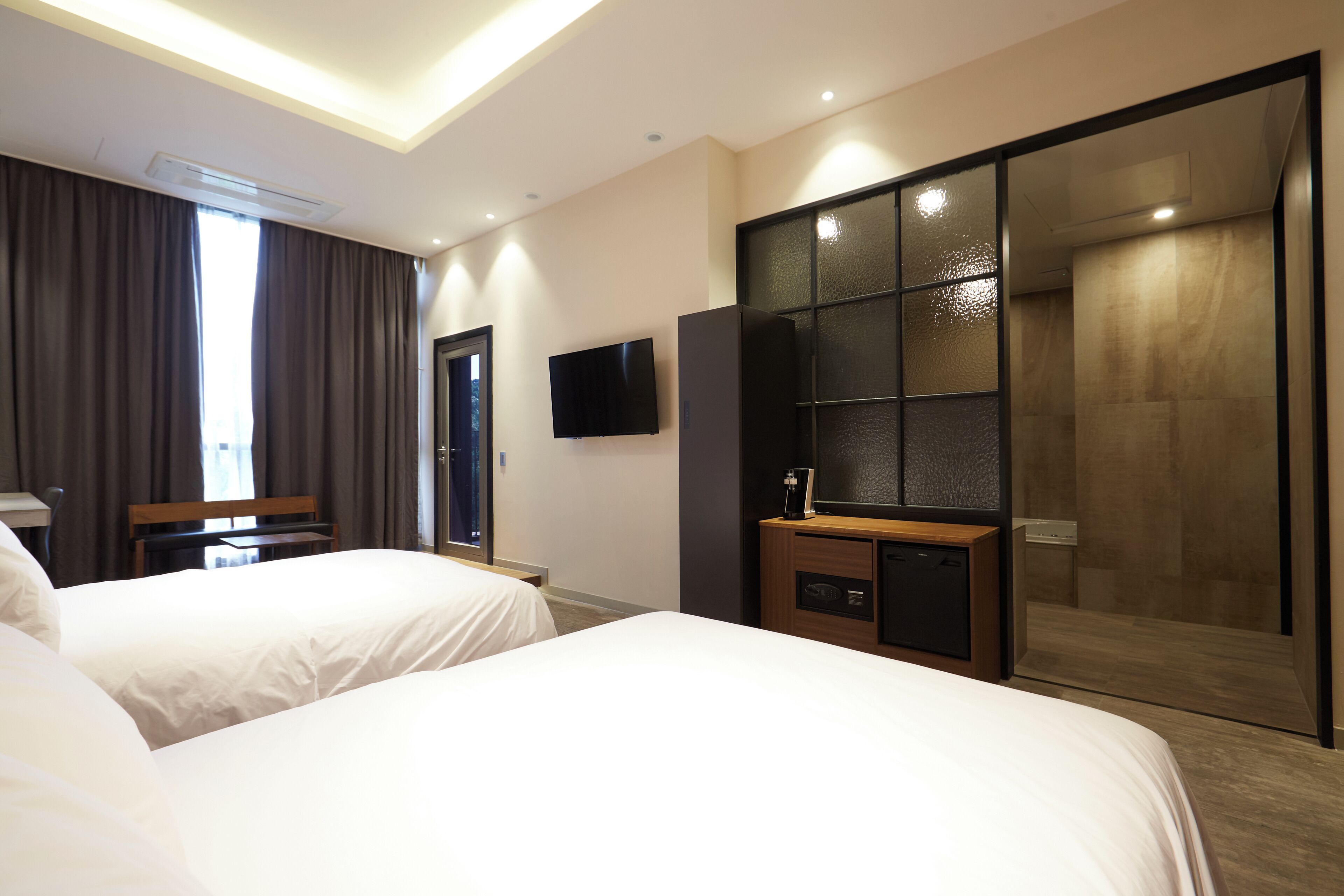 Habitación de hotel con dos camas, un escritorio, un televisor y una puerta corredera que da a una zona de ducha.