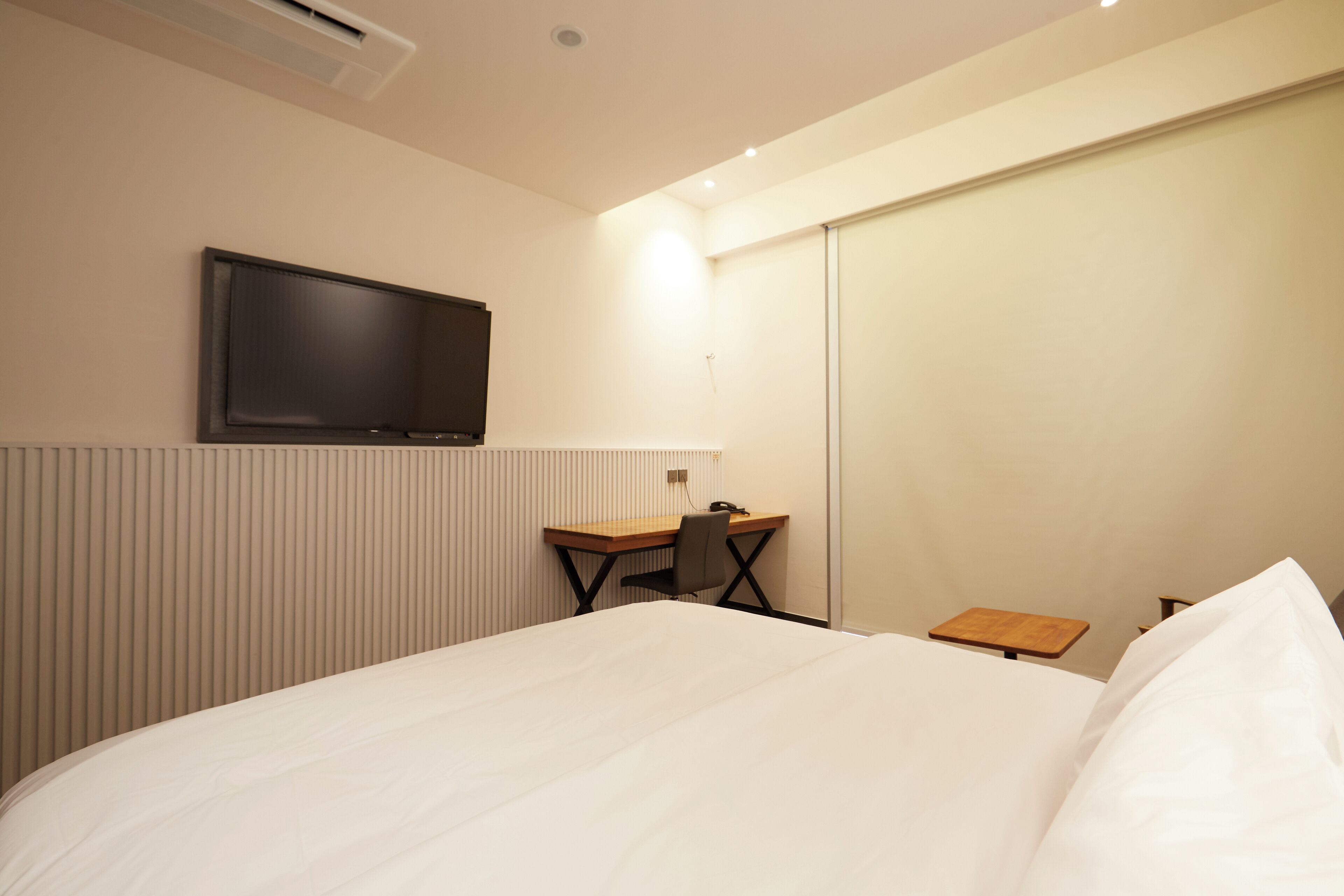 A hotel room with a bed, a desk, a chair, a television, and a small table.