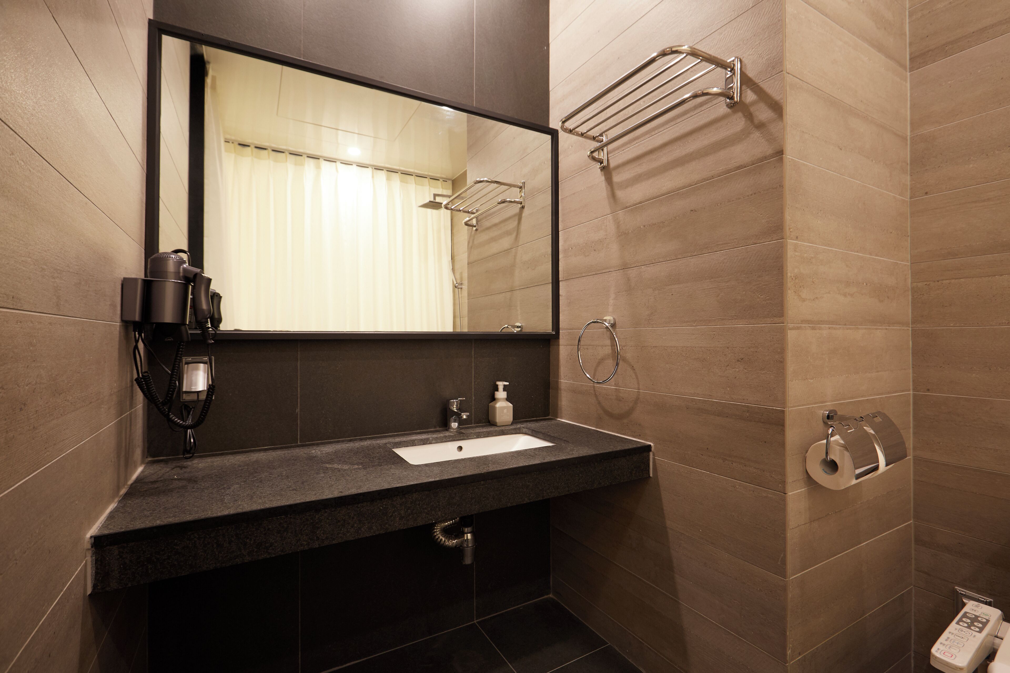A modern bathroom with a dark granite countertop, a mirror, a towel rack, a toilet paper holder, and a shower area.
