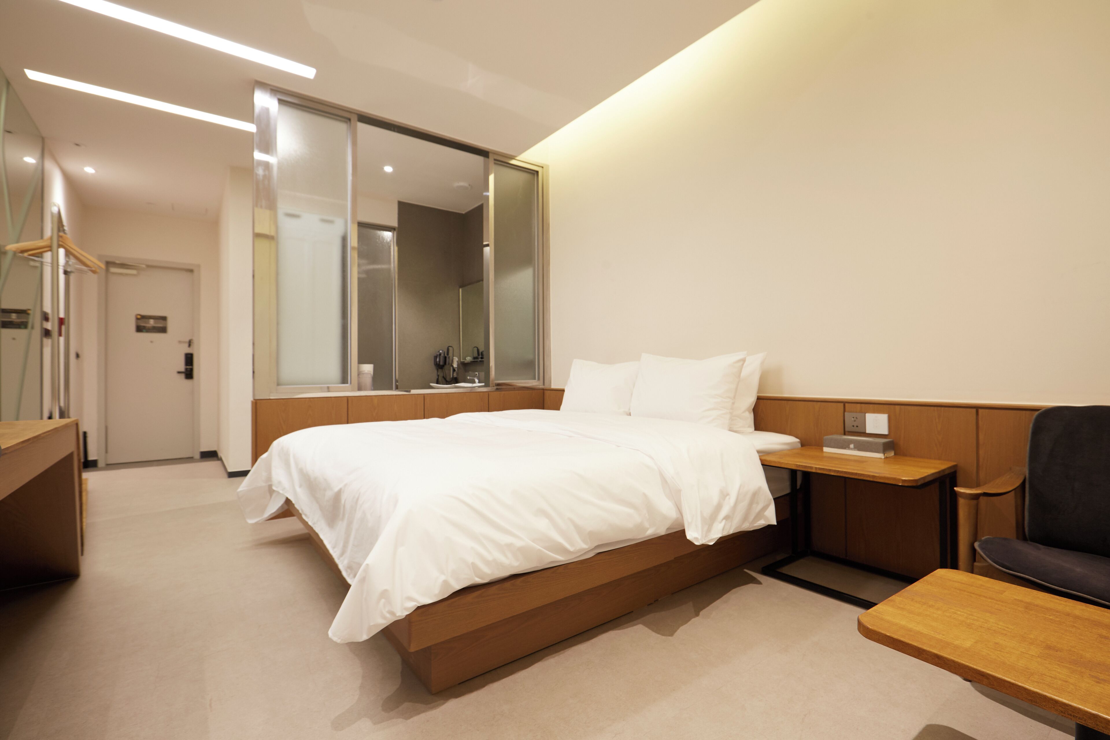 A modern hotel room with a large bed, a wooden nightstand, a desk, and a chair.