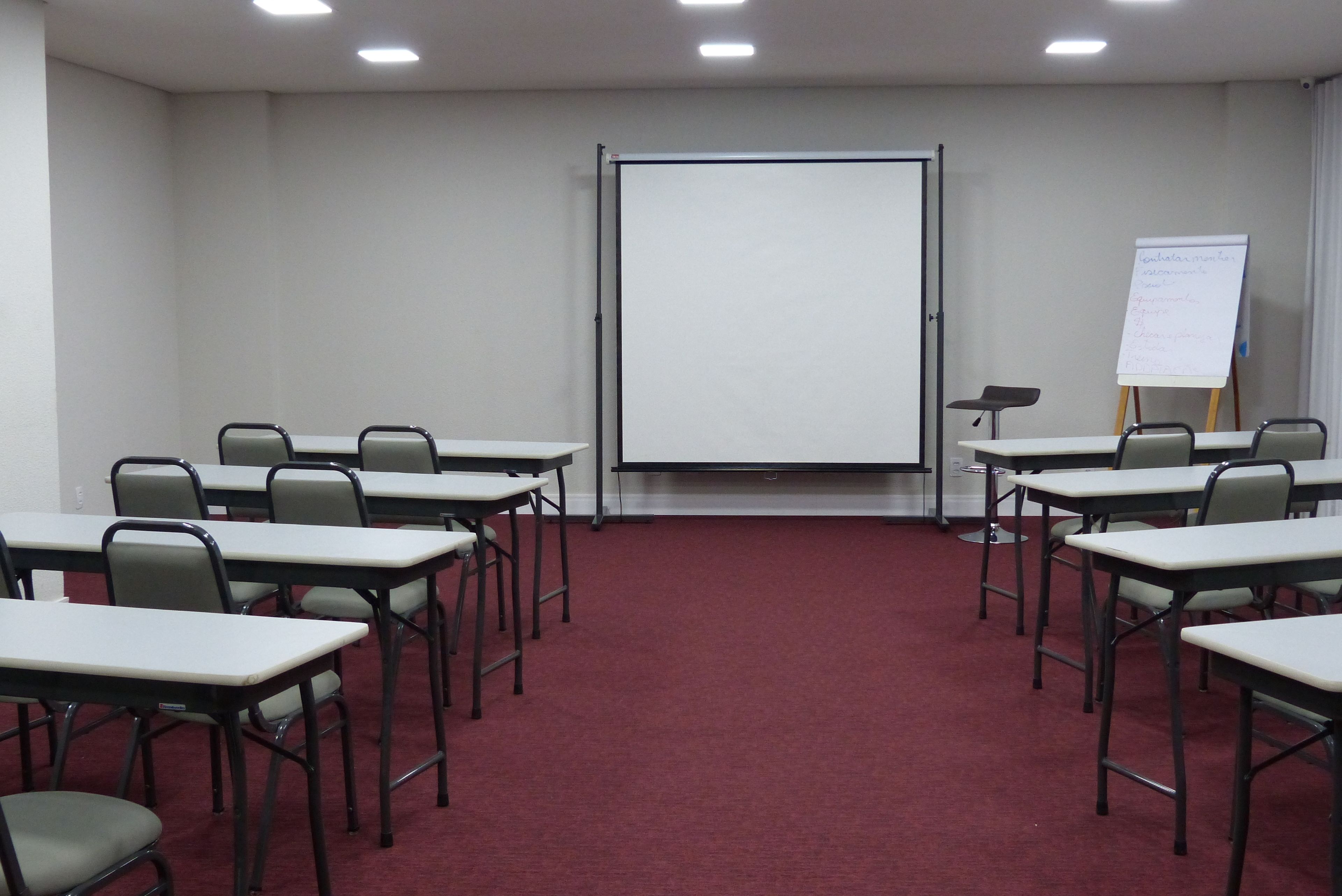 Una sala de conferencias con una pizarra, un rotafolio y varias mesas con sillas.