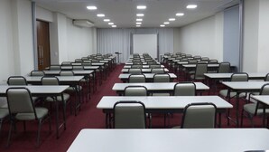 A conference room with rows of tables and chairs, a projector screen, and a door on the left. - Hotel 10 Palmas (Palmas)