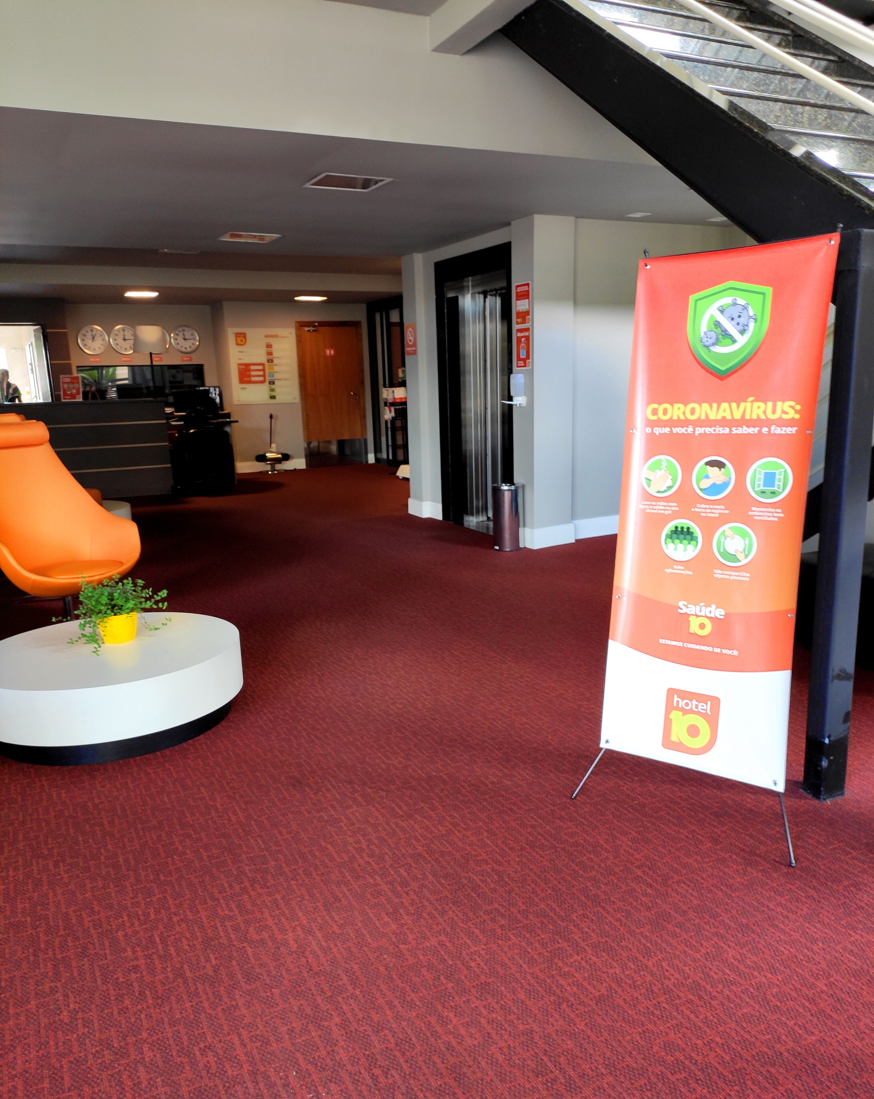 A hotel lobby with a red carpet, a reception desk, a digital clock, and a sign about coronavirus.