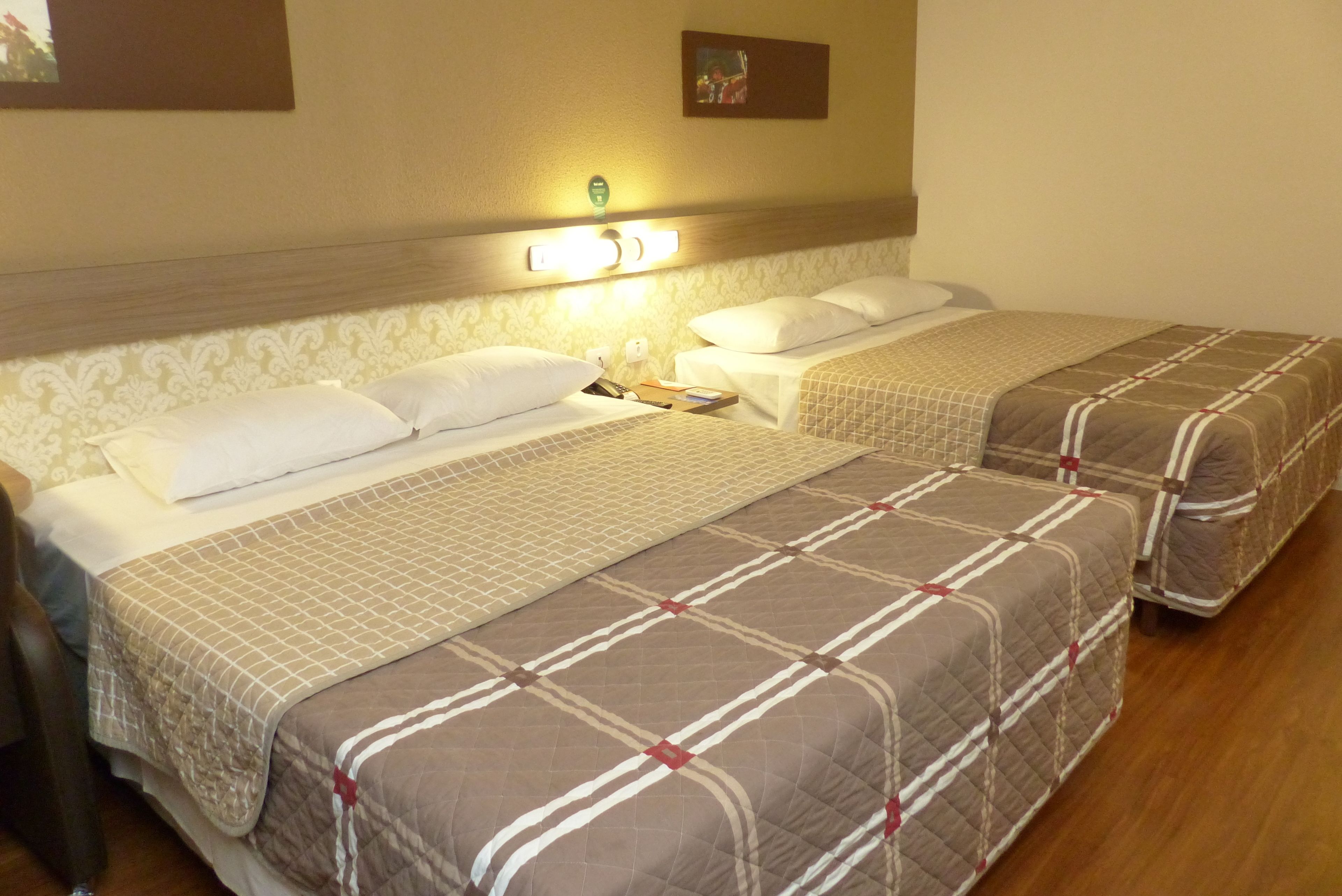 Une chambre d’hôtel avec deux lits, chacun recouvert d’une courtepointe matelassée et agrémenté d’oreillers. On y trouve une table de chevet avec une lampe, ainsi qu’une petite table sur laquelle sont posés un livre et une télécommande.
