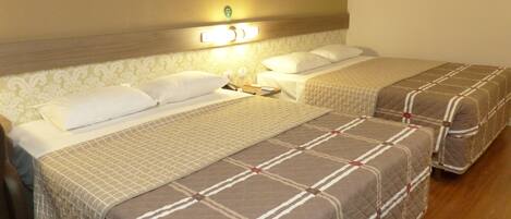 Une chambre d’hôtel avec deux lits, chacun recouvert d’une courtepointe matelassée et agrémenté d’oreillers. On y trouve une table de chevet avec une lampe, ainsi qu’une petite table sur laquelle sont posés un livre et une télécommande.