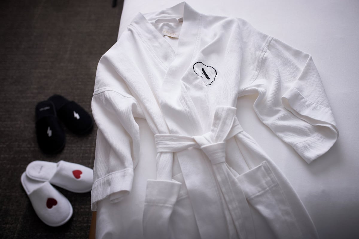 A white robe with a heart design, a pair of white slippers with red hearts, and a black cap with a lightning bolt.