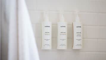 Tres botellas de gel de ducha Lather sobre una pared de azulejos blancos.