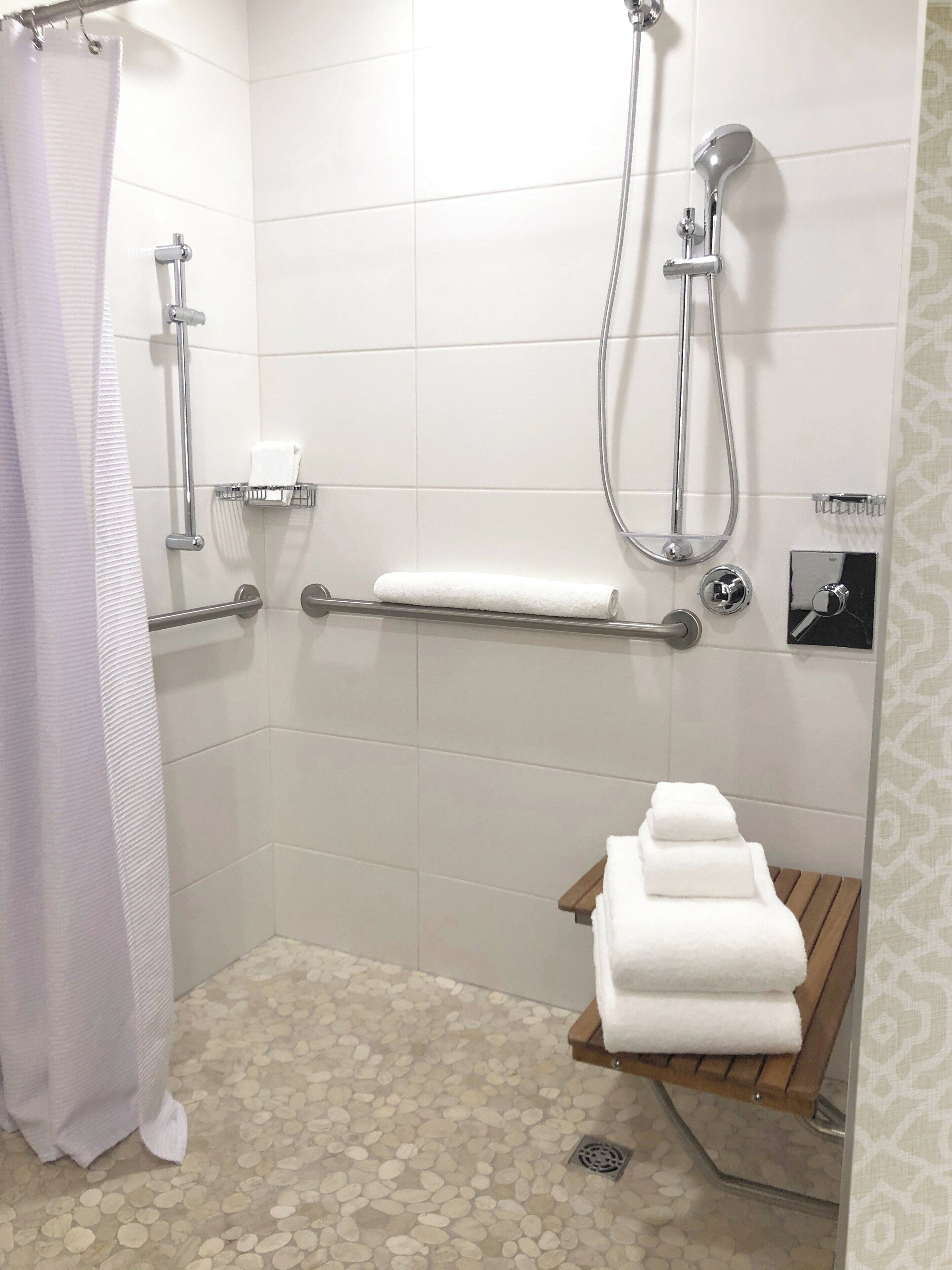 A shower area with a grab bar, a towel rack, and a wooden shelf with towels.