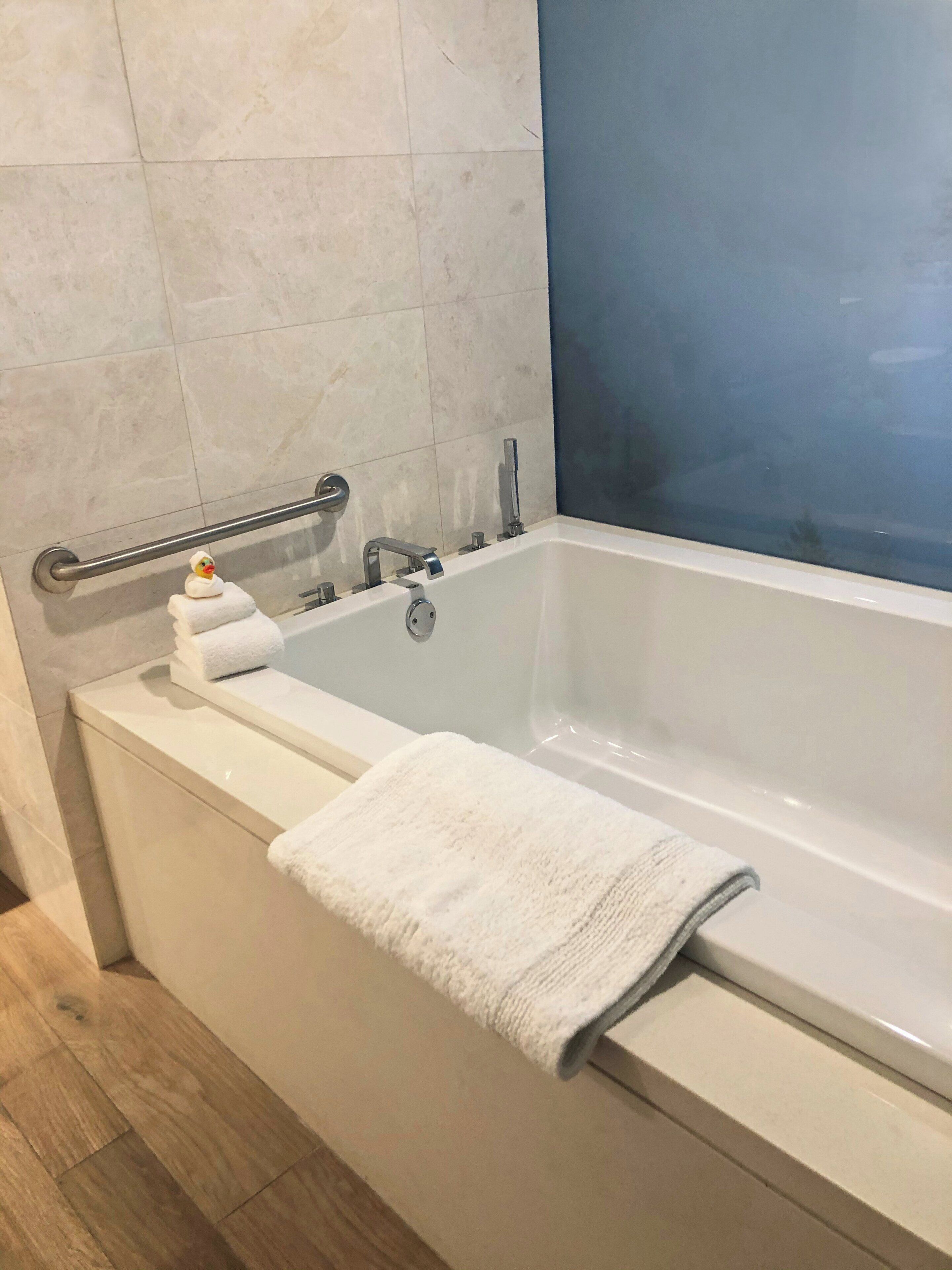 A modern bathroom with a white bathtub, a glass shower enclosure, and a handrail.