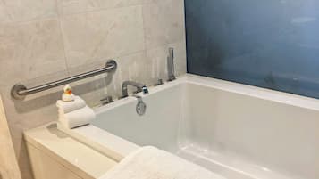 A modern bathroom with a white bathtub, a glass shower enclosure, and a handrail.