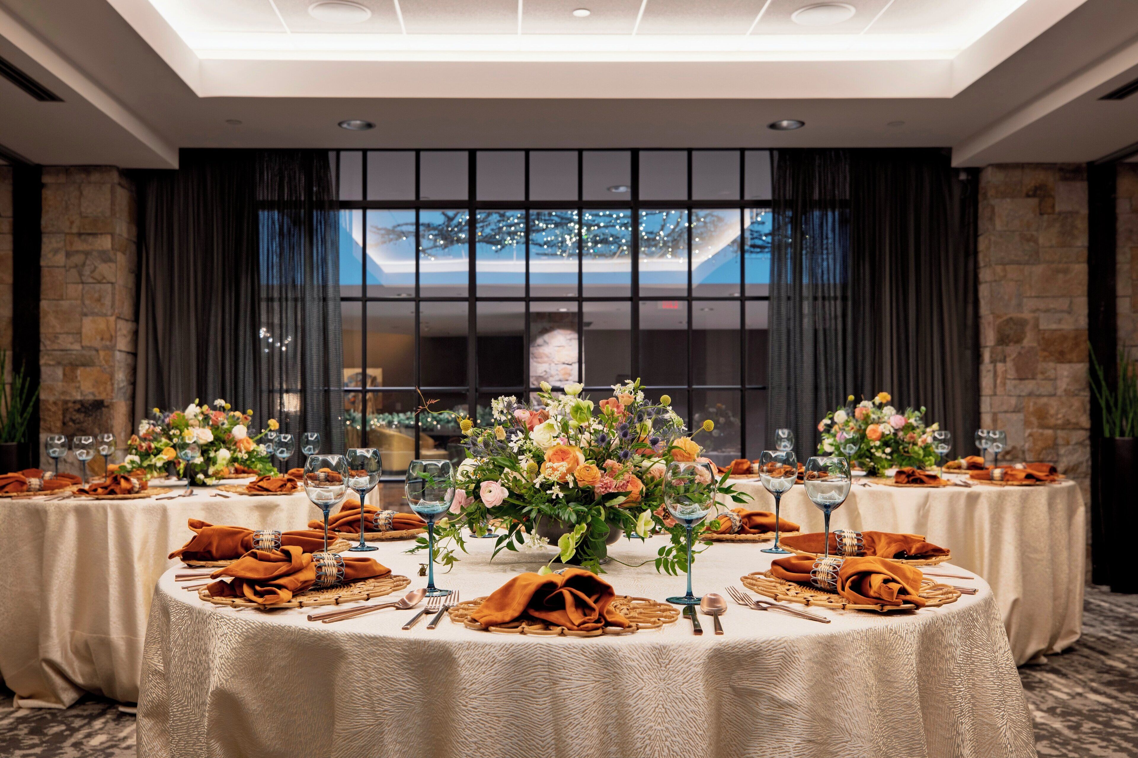 A banquet hall with round tables set for a formal event, featuring floral centerpieces and elegant table settings.