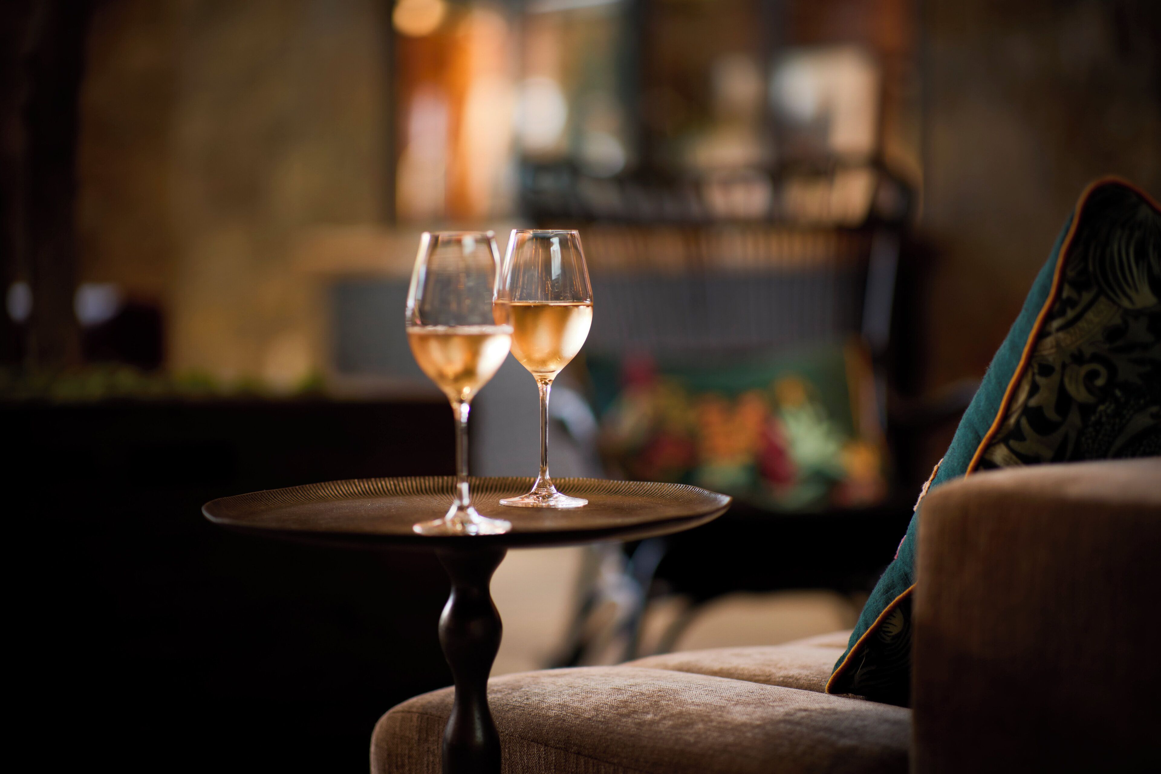 Two wine glasses on a table in a dimly lit room with a blurred background.