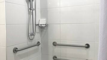 Een moderne badkamer met witte tegels, een badkuip, een douche met handdouche en veiligheidsbeugels.