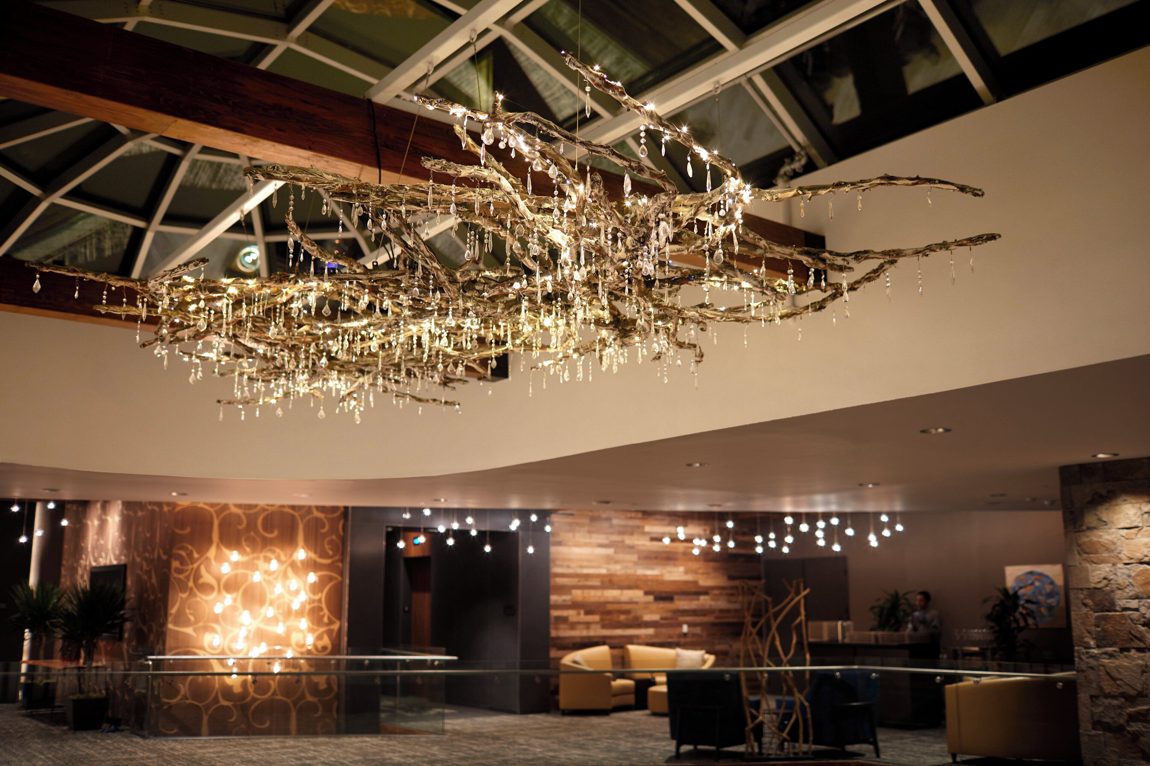 A modern lobby with a unique chandelier, seating area, and a glass ceiling.