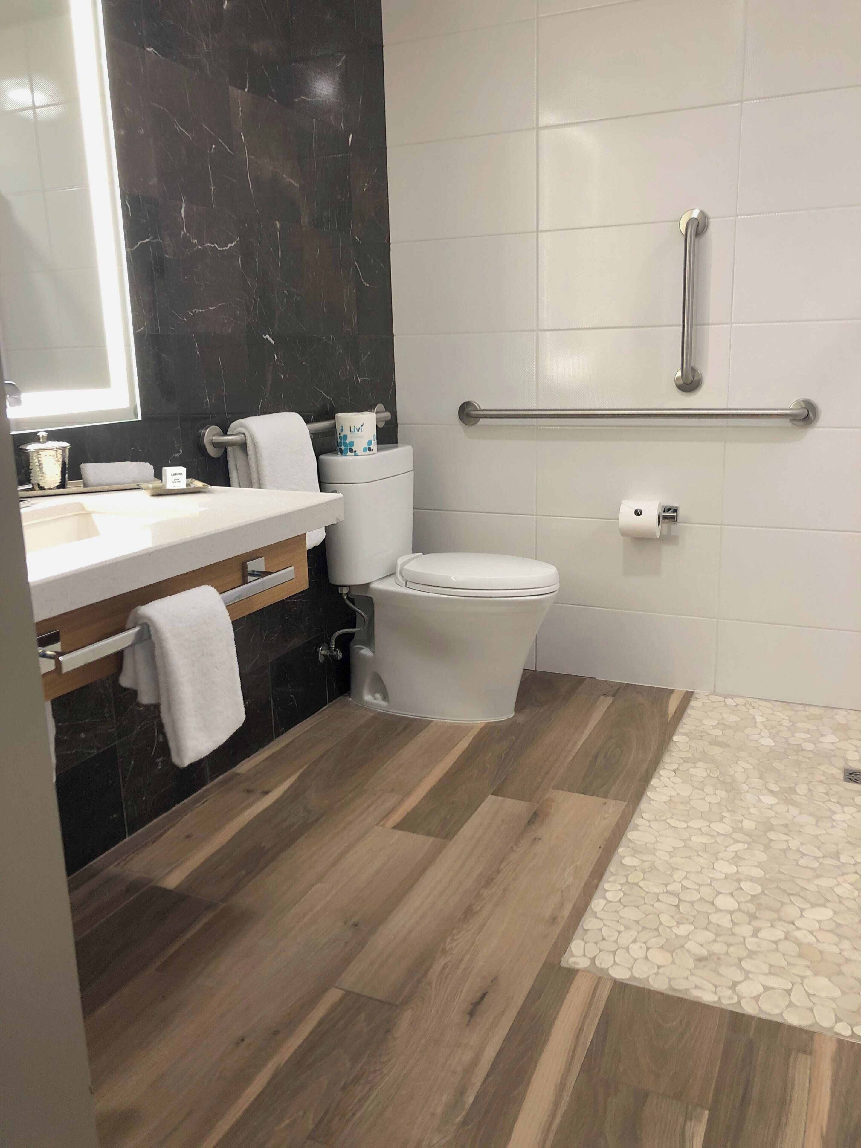 Une salle de bain moderne avec un pare-feu en marbre, un meuble-lavabo en bois, des toilettes blanches et une barre d’appui.