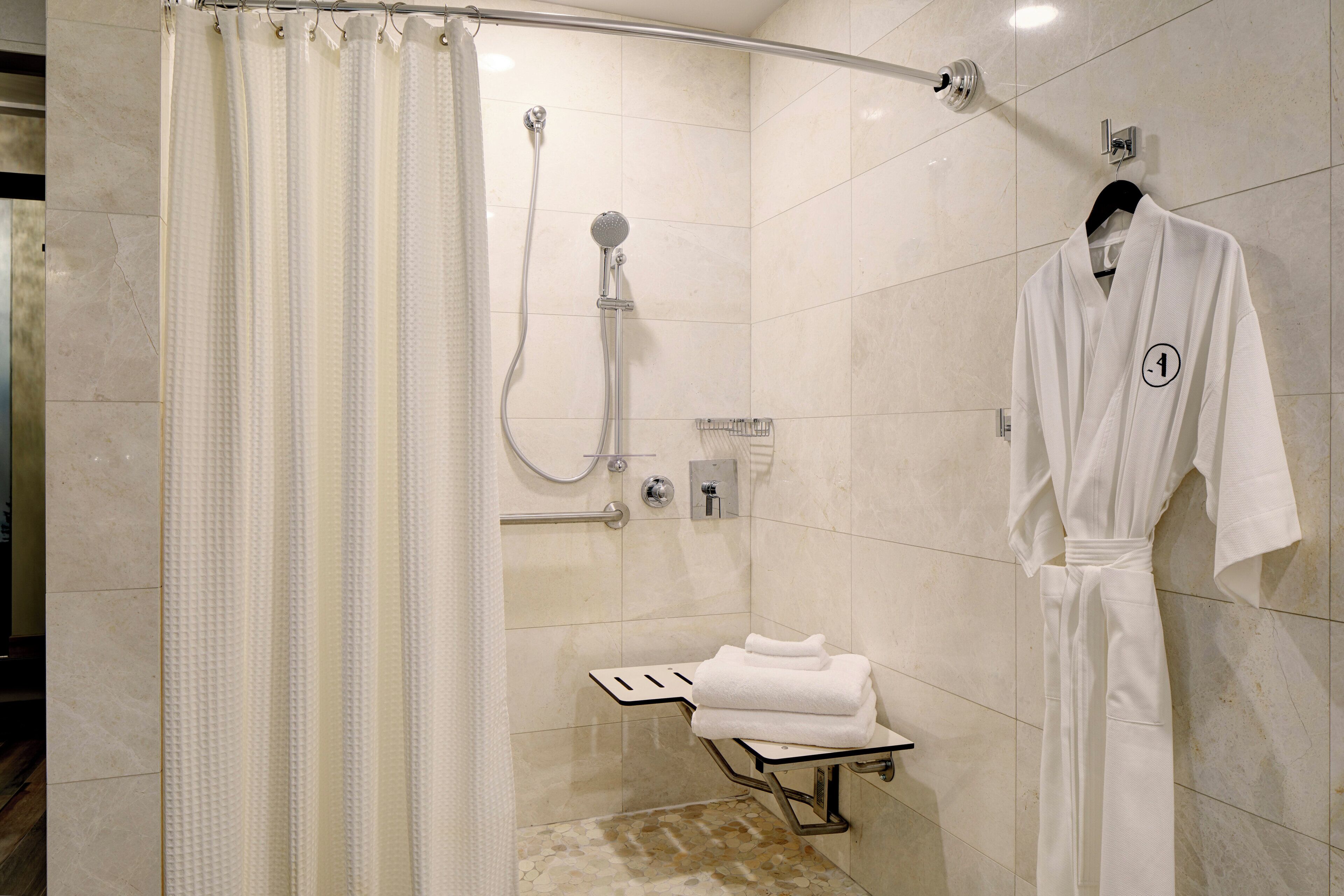 Un baño moderno con cabina de ducha de vidrio, perchero y asiento de ducha de cristal.